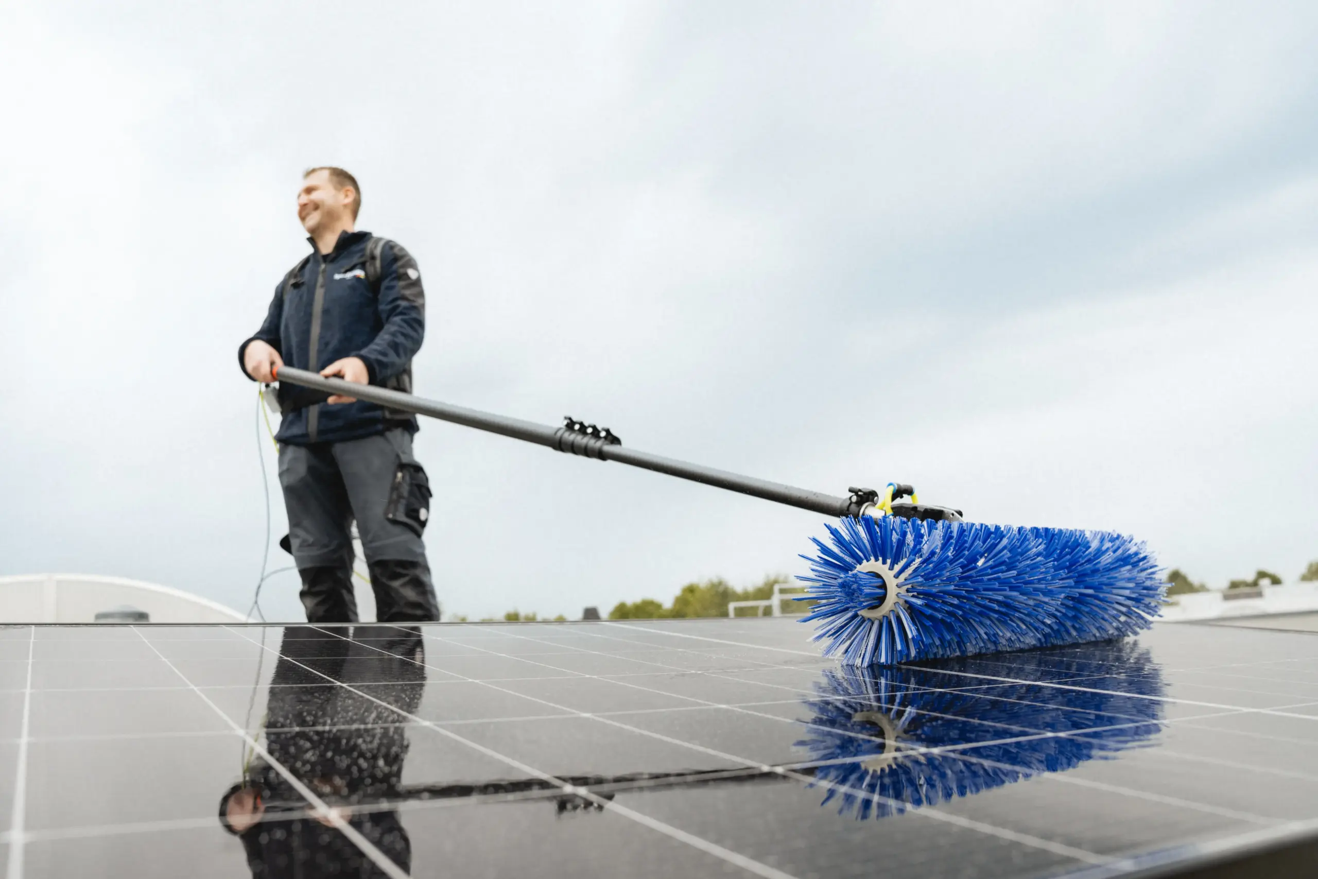 man using solar brush to clean solar panel at roof